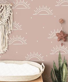 the wallpaper in this nursery room is pink and has sun, clouds, and stars on it