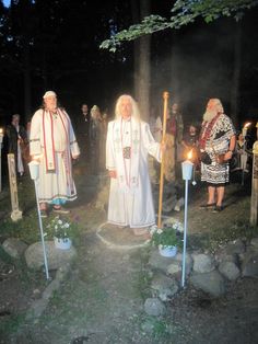 two men in white robes standing next to each other with candles on the ground near them