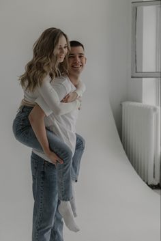 a man holding a woman on his back in front of a white wall and window