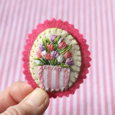 a hand holding a small flower pot on top of a pink and white striped cloth