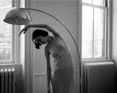 a woman standing in front of a lamp on top of a wooden floor next to a radiator