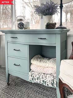 a blue dresser with two drawers and a clock on it's top, in front of a window