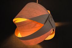 a wooden lamp hanging from a hook on a black wall with light coming through it