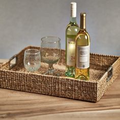 two bottles of wine are sitting in a wicker tray on a wooden table next to glasses