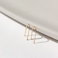 14k solid gold wire formed into arch shaped earrings with one hammered end, photographed on a white table leaning on a white dish Jewelry Details, Forever Jewelry, Leather Box, Solid Gold Jewelry, Silver Spring, Fine Jewelry Collection, Pendant Bracelet, Bridal Gifts, Sensitive Ears