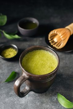 a cup filled with green tea next to two spoons