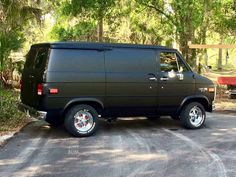 a black van parked on the side of a road in front of trees and bushes