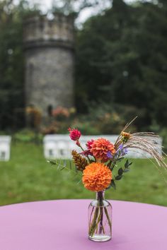 a vase filled with flowers sitting on top of a purple table covered in white chairs