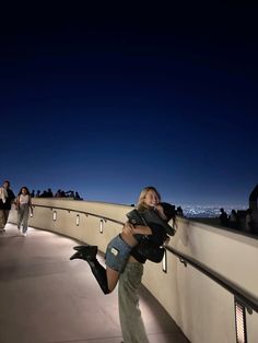 a woman carrying a man on her back as they walk along a bridge at night