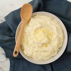 a bowl filled with mashed potatoes and butter on top of a blue napkin next to a wooden spoon