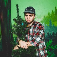 a man standing next to a tree in front of a green wall