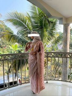 a woman in a pink dress is standing on a balcony with palm trees behind her