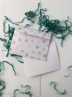 an envelope and some green string on a white surface with flowers in the corner,