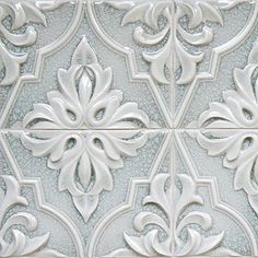 an ornate tile pattern with white and silver accents on the side of a wall or floor