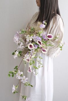 a woman holding a bouquet of purple and white flowers in her hands with long dark hair