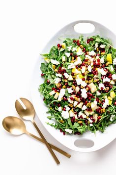 a white bowl filled with salad next to two gold spoons