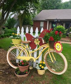 a yellow bicycle with flower pots on the front and back wheel is parked in front of a white picket fence