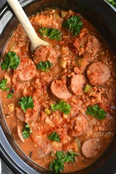 a crock pot filled with meat and vegetables next to a wooden spoon on top of a table