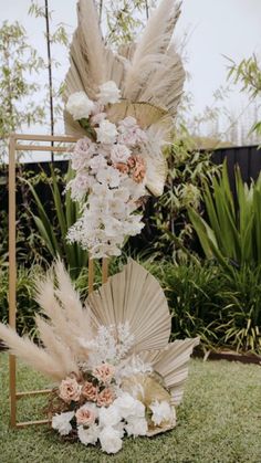 an arrangement of flowers and feathers on a stand in the grass near some bushes,