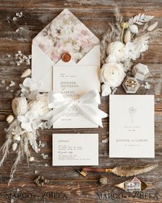 the wedding stationery is laid out on a wooden table with white flowers and feathers