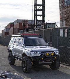 an suv parked on the side of a road next to a tall building with lots of shipping containers behind it