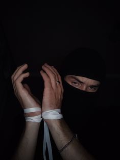 a man wearing a black mask and white bandages on his hands is holding something in the dark