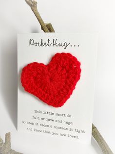 a red crocheted heart shaped brooch sits on a white card that reads, pocket hug