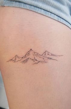 a woman's thigh with a small mountain tattoo on the back of her leg