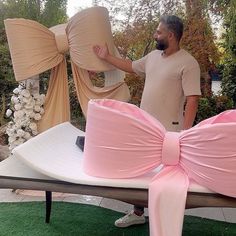 a man standing next to two giant bows on top of a bed in the grass