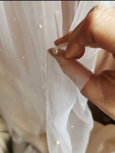 a person holding something in their hand near a white curtain with pearls on it,