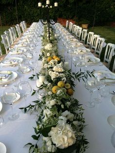 the long table is set with white and yellow flowers, greenery, and candles