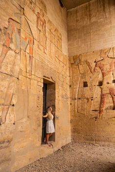 a woman in a white dress standing at the entrance to an ancient building with paintings on it