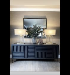 a black dresser with two lamps and a mirror on it's sideboard in a living room