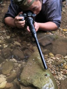 a man laying on top of a rock with a camera in his hand next to water