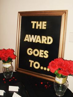 two vases filled with red flowers sitting on top of a table next to a sign