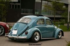 an old blue vw bug parked in front of a red car on the street