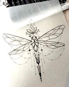 a drawing of a dragonfly on paper next to some markers and pencils in the background