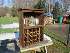 a wooden wine rack with bottles in it sitting on a picnic table next to a tree