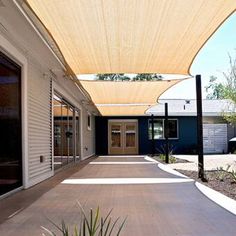 an outdoor patio with sun shade covering the walkway and door to the back yard area