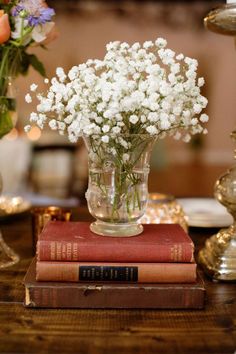 flowers in a vase sitting on top of two books next to a candle and some candles