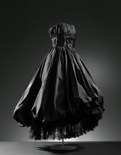 Balenciaga Evening dress in black silk taffeta  1952 Ca.  Longer at the back than the front and cut at waistline. The bodice has a strapless neckline and is reinforced with boning. Lined with rayon gros de Naples. The outside is decorated with vertical draping, secured at the centre of the bust with ribbon and bow appliqués. The skirt is very gathered and puffed, made of nylon tulle and a gros de Naples petticoat reinforced with metal hoops. The frilly petticoat has two Chantilly-type, machine-made lace frills at the bottom. Both frills have a black nylon ribbon. The dress fastens on the left side with a zip.   Made in Paris for the 1952 spring collection, this dress has marvellous shapes and details. In 1951, Balenciaga created a dress for his autumn collection, presented as number 130, w Balenciaga Dress, Vintage Haute Couture, Jacques Fath, Charles James, Silk Taffeta