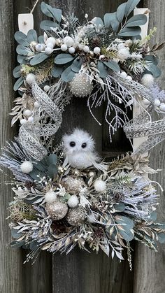 a wreath with an owl on it hanging from the side of a wooden door, decorated with greenery and white balls