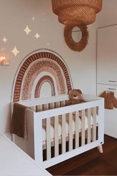 a white crib with a brown teddy bear in it and a rainbow mural on the wall