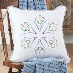 a white pillow sitting on top of a wooden chair next to a blue crocheted blanket