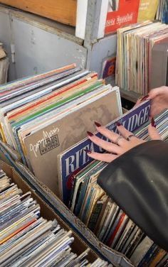 a woman is looking at records in a record store with her hand on the top of an old record player