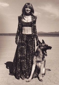 a woman standing next to a dog on top of a sandy beach