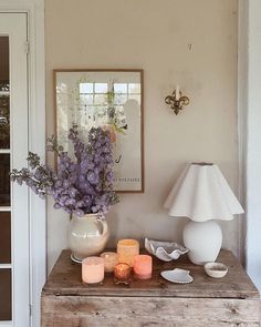 a wooden table topped with a vase filled with purple flowers next to a white lamp