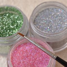 three different colored glitters in small jars with a brush