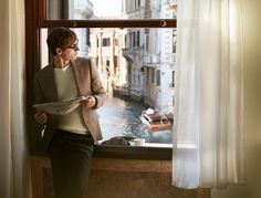 a woman standing in front of a window looking out at the water and boats outside