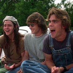 three young men sitting on the ground laughing